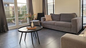 A living room with a grey sofa, a round coffee table with a vase and figurines, and a painting on the wall. - Nature cottage Abcoude - Green Stay Buitenhuis (Abcoude)