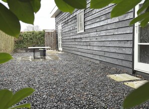 A gravel patio with a table and chairs, a wooden fence, and a house with a window. - Nature cottage Abcoude - Green Stay Buitenhuis (Abcoude)
