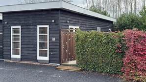 A modern black building with a flat roof, a wooden door, and a small porch. - Nature cottage Abcoude - Green Stay Buitenhuis (Abcoude)