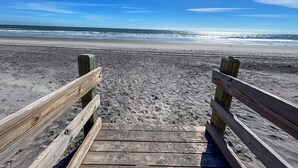 Une promenade en bois menant à une plage, avec un ciel dégagé.