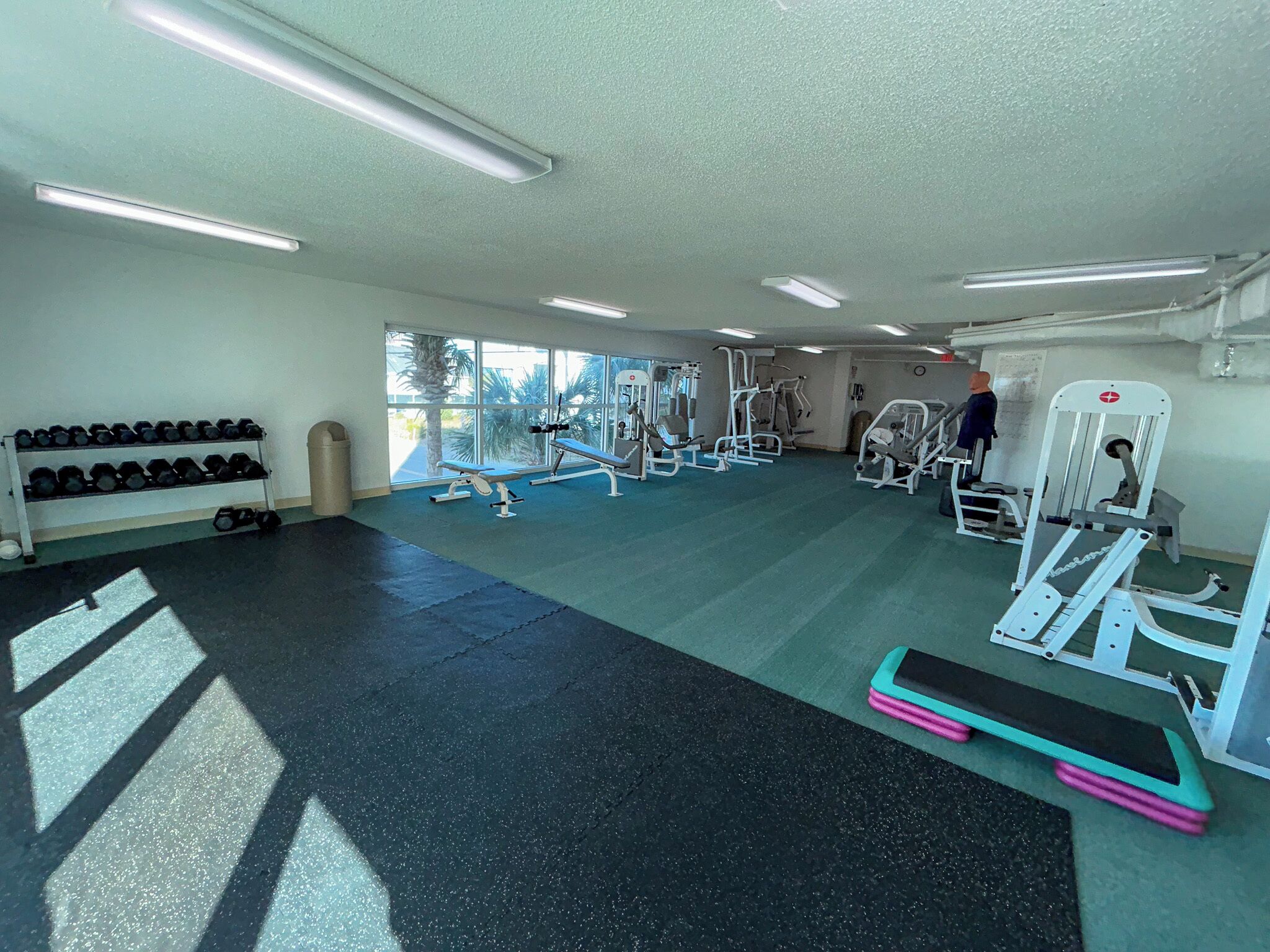 Un gimnasio con equipo de ejercicio, un perchero para zapatos y amplias ventanas.
