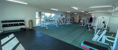 Un gimnasio con equipo de ejercicio, un perchero para zapatos y amplias ventanas.
