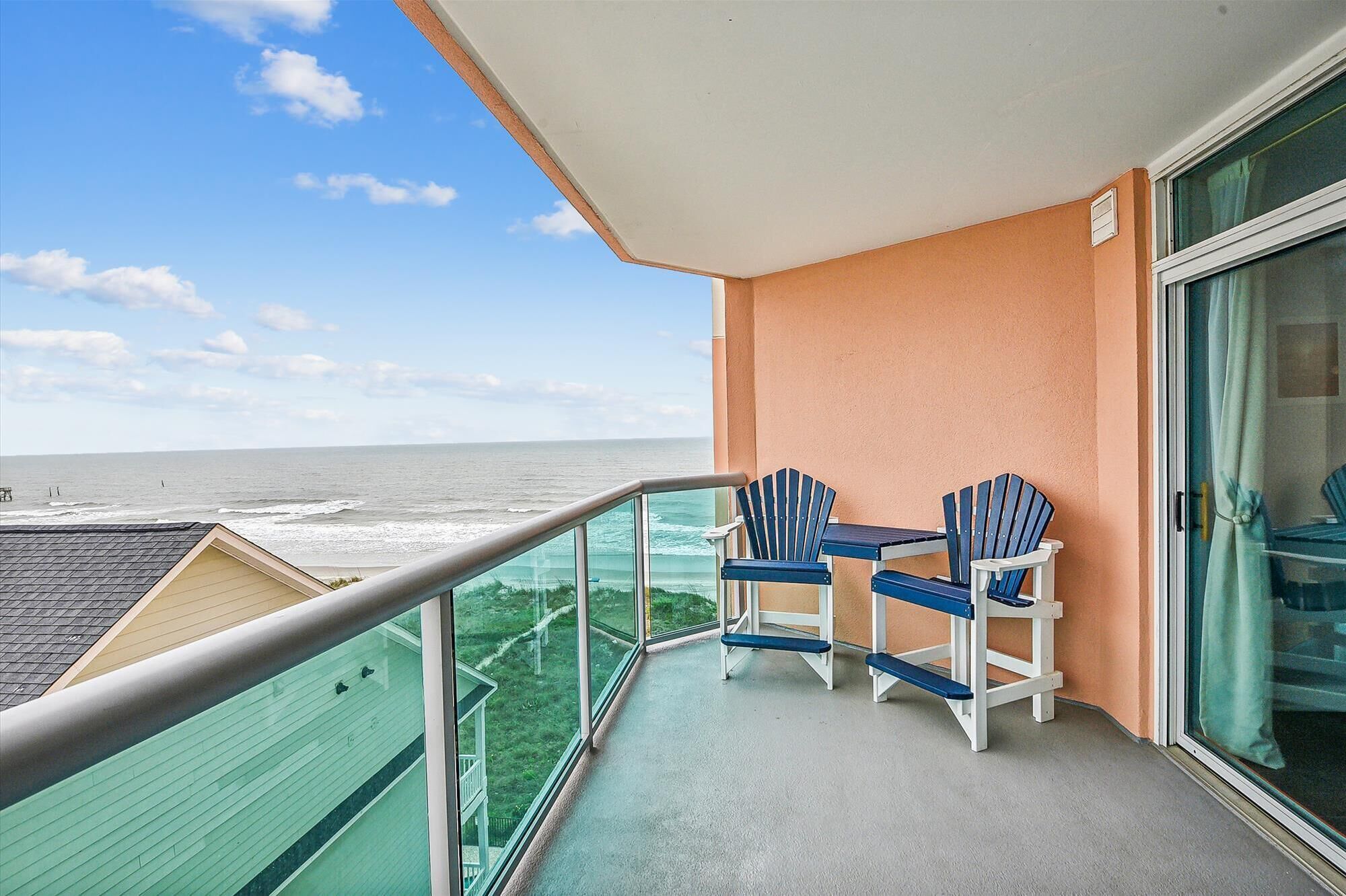 Een balkon met uitzicht op de oceaan, twee Adirondack stoelen en een glazen deur.