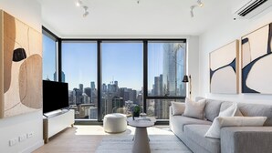 Ein modernes Wohnzimmer mit großem Fenster, einem Flachbildfernseher, einem grauen Sofa und einem runden Couchtisch.