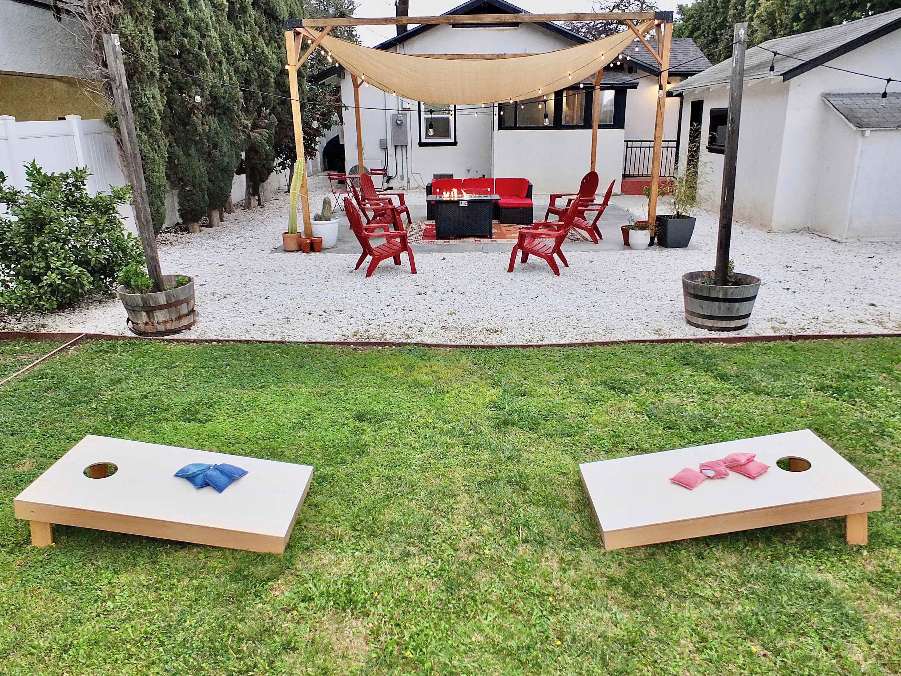Patio trasero con un área de estar techada, dos juegos de jardín y plantas en macetas.