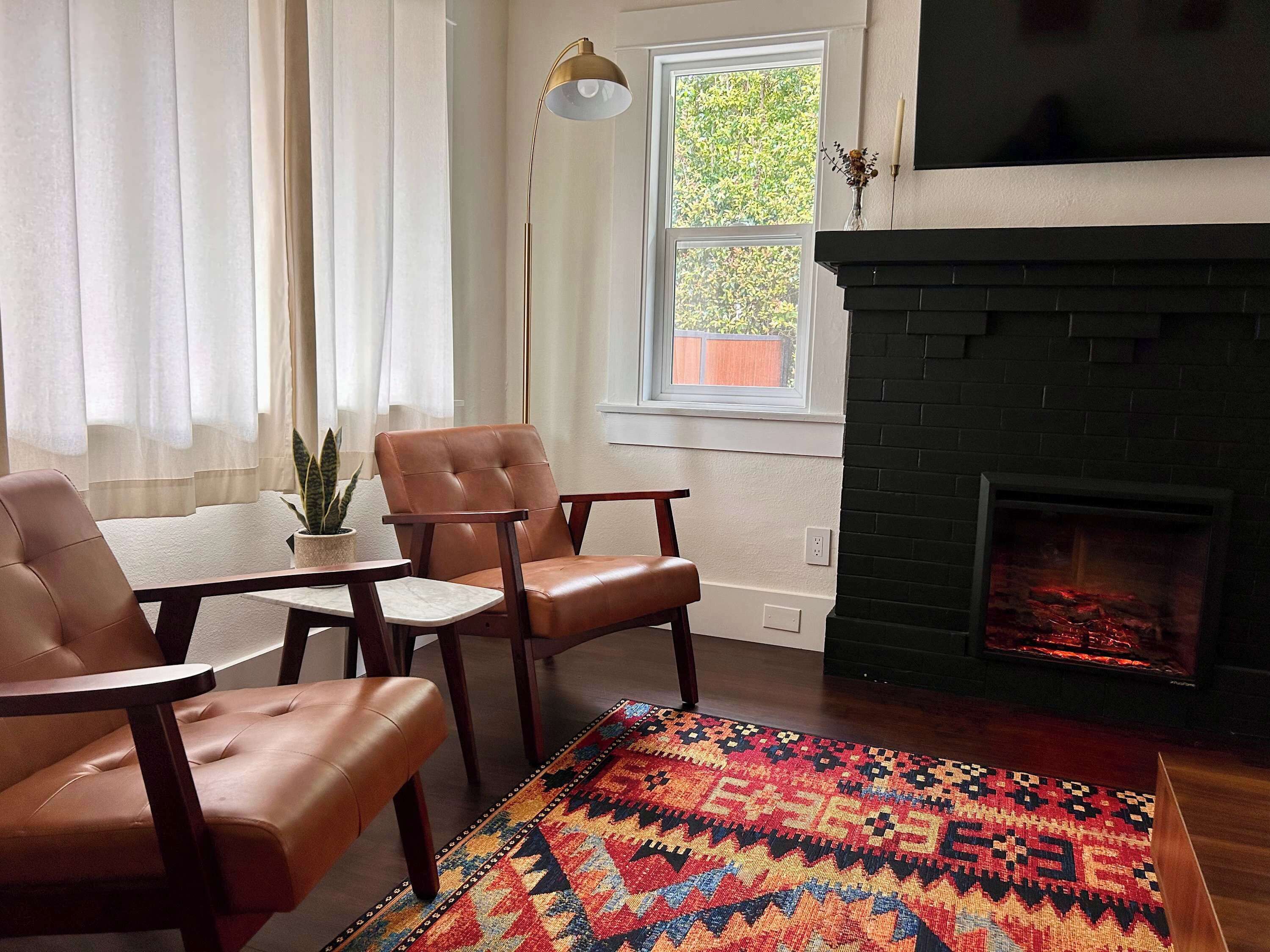 A living room with a fireplace, leather chairs, a small table, and a colorful rug.