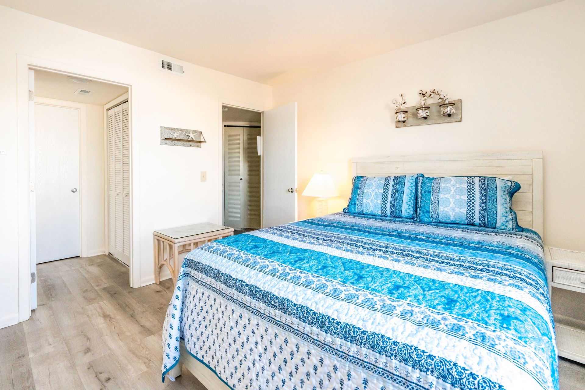 Un dormitorio con una cama, una mesita de noche, una lámpara y un aplique de pared.