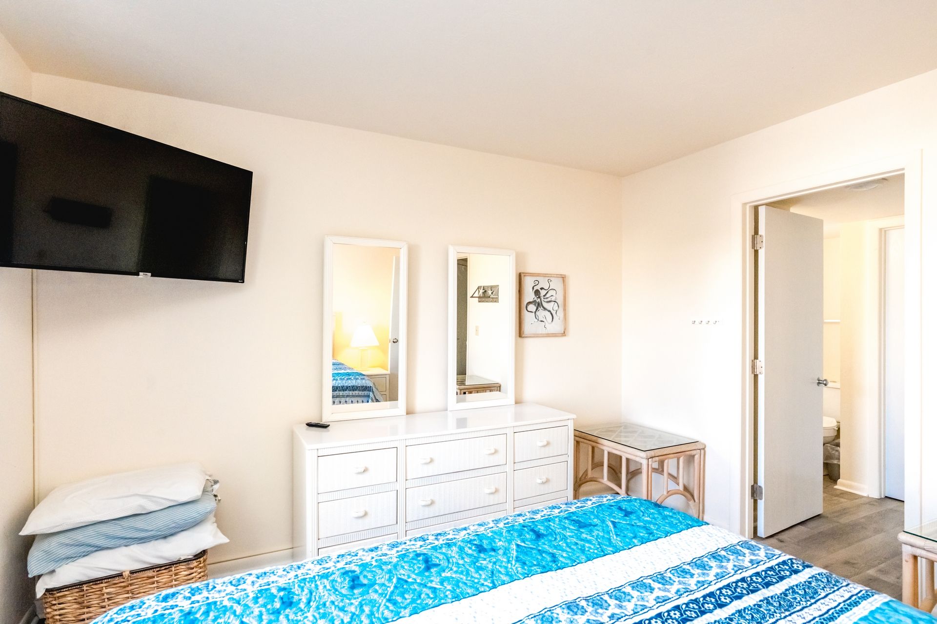 A bedroom with a bed, a dresser, a television mounted on the wall, and a door leading to another room.