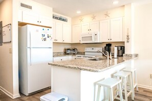 A kitchen with white cabinets, a refrigerator, a microwave, a toaster, and a coffee maker. - Joanie's Gem - 1st Floor Surf Condo - Sleeps 6! (Surf City)