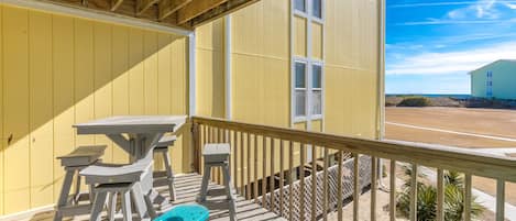 A wooden deck with a yellow building, a table, and two chairs.