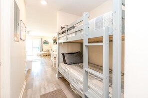 Een slaapkamer met een stapelbed, een bureau en stoel, een raam en een deur.