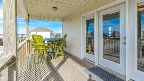 A covered outdoor area with a table and chairs, a wooden deck, and a view of the ocean and buildings. - Knot Too Shabby - Quaint Home with Covered Porches on Quiet Street (North Topsail Beach)
