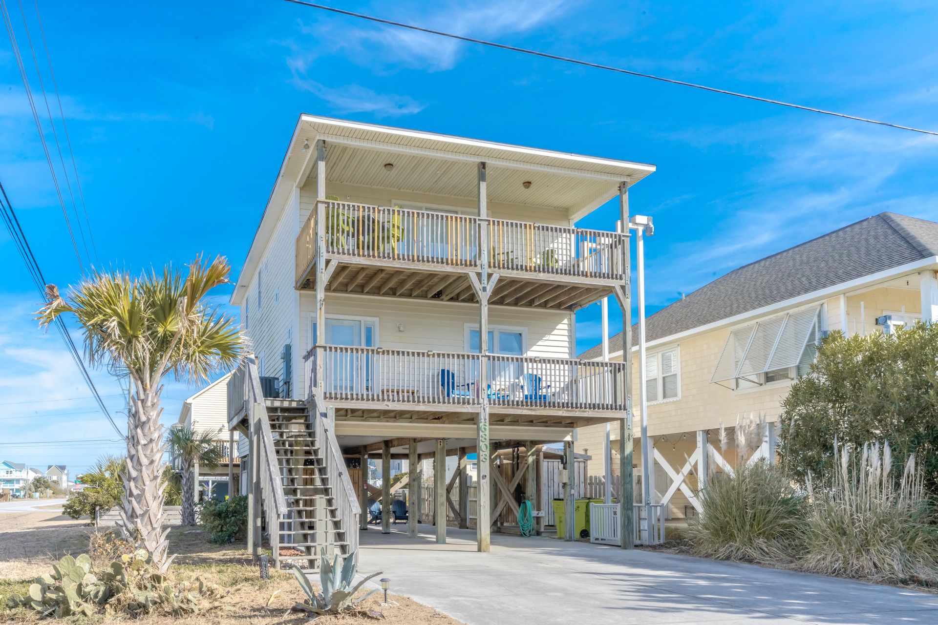 A multi-story beachfront property with a covered outdoor area and a staircase leading to the upper floors.
