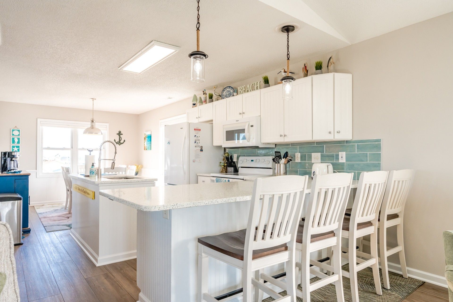 A kitchen with white cabinets, a central island with bar stools, a microwave, and a stove.