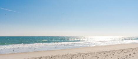 A beach with a clear sky, calm sea, and visible footprints on the sand.