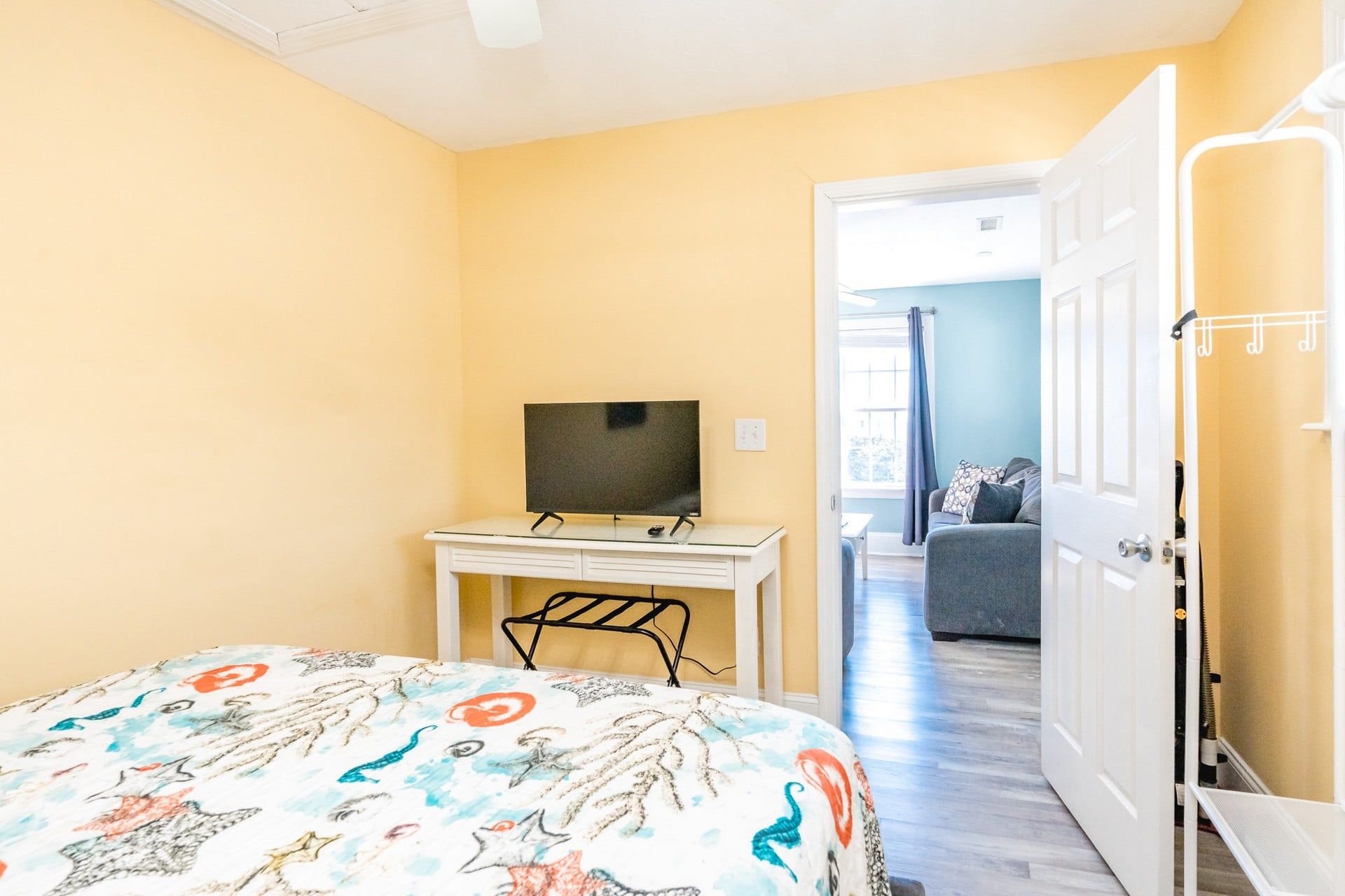 A bedroom with a bed, a desk with a television, and a door leading to another room.
