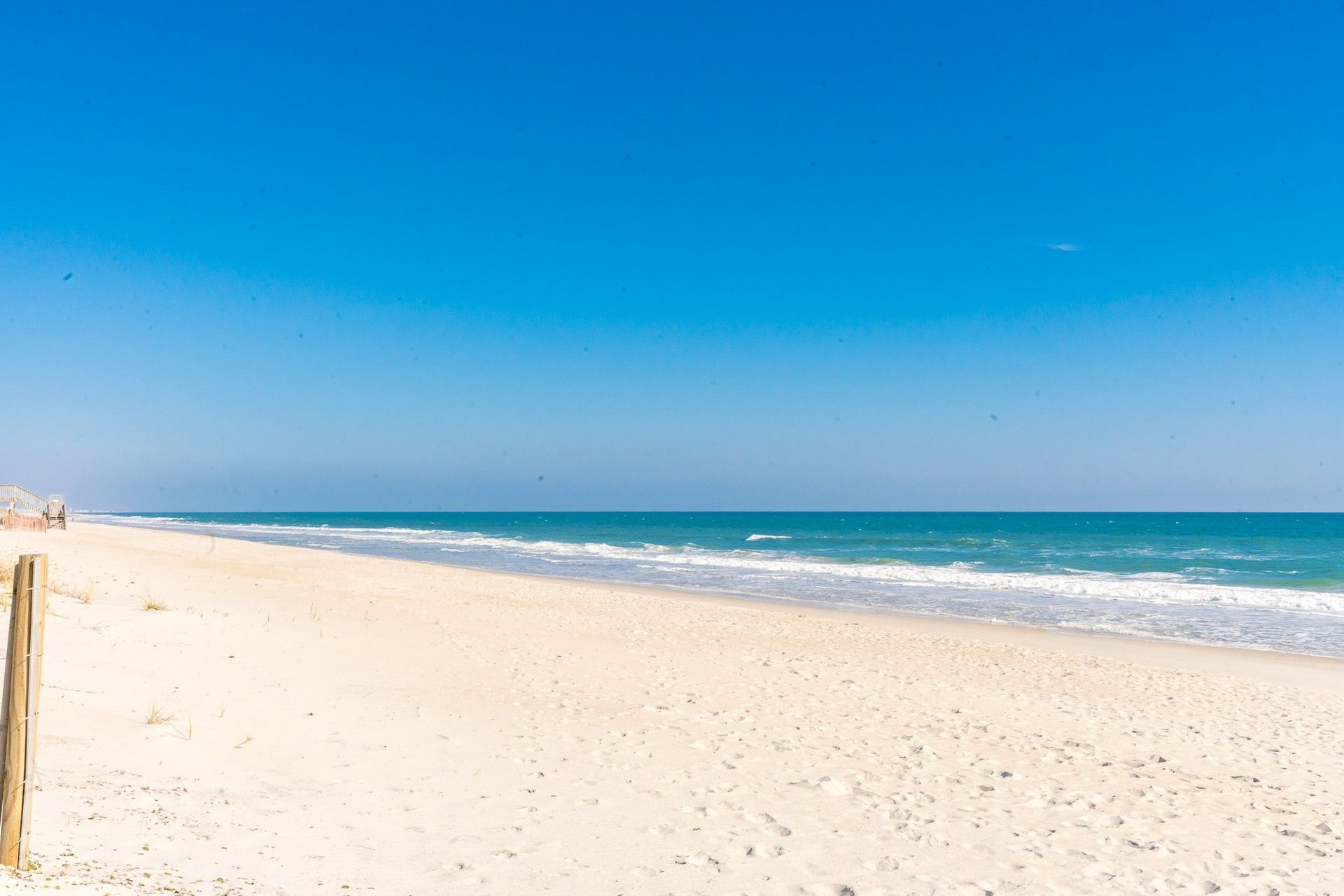 A beach with a wooden fence and a clear blue sky.