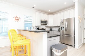 A modern kitchen with white cabinets, stainless steel appliances, and a central island with yellow chairs. - 613A Follow the Sun - Upscale 4 BR Home Surf City; Dogs welcome! (Surf City)