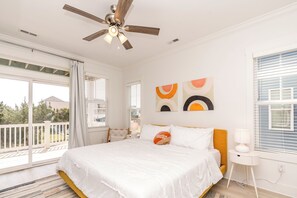 A bedroom with a bed, ceiling fan, artwork, and a view of the outdoors.