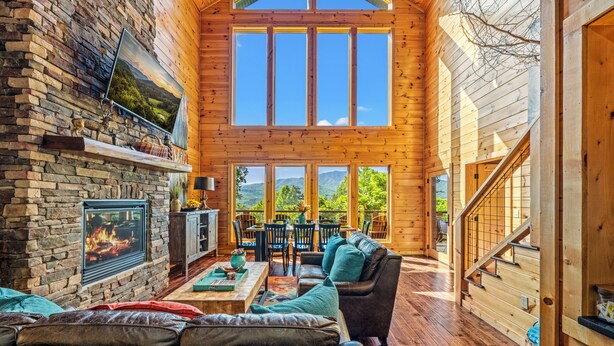 Ein Blockhaussalon mit Kamin aus Stein, Holzwänden, einem Essbereich und einer Treppe.