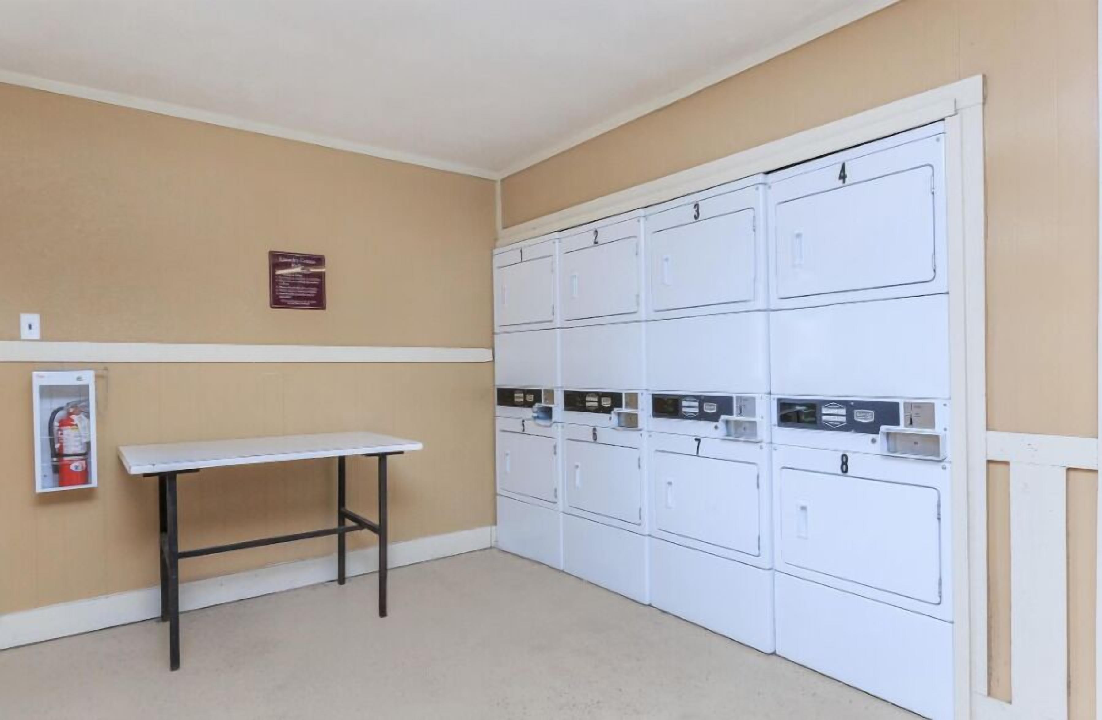 A laundry room with white lockers numbered 1 to 8, a fire extinguisher, and a table.