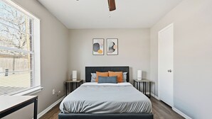 Et soveværelse med seng, sengeborde, ventilator i loftet og billedkunst på væggen.