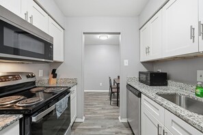 A modern kitchen with white cabinets, a black microwave, a stove, and granite countertops.