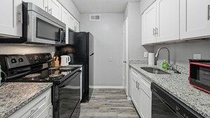 A modern kitchen with white cabinets, a stainless steel stove, a black refrigerator, a granite countertop, and a built-in microwave. - Denton pad with 2BR comfort (Denton)