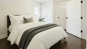 Ein modernes Schlafzimmer mit einem großen Bett, weißen Wänden und dunklem Boden.