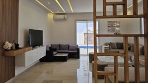 A modern living room with a flat-screen TV, a sofa, and a wooden partition. - Luxurious Villa Rental in Houmt Souk, Djerba - Perfect Family Retreat (Houmt Souk)