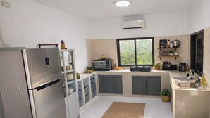 Une cuisine moderne équipée d’un réfrigérateur, d’un four à micro-ondes et d’une cuisinière intégrés. Une fenêtre laisse entrer la lumière naturelle et offre une vue sur la verdure environnante.