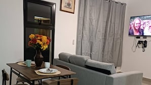 A living room with a grey sofa, a dining table with chairs, a vase of flowers, and a television on the wall. - Luxury and Peace Near Downtown Puntacana (Punta Cana)