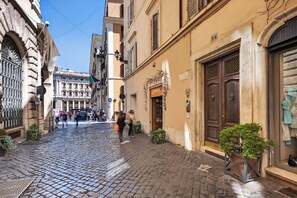Una strada acciottolata fiancheggiata da edifici storici, un negozio con insegna e una piccola pianta in vaso.
