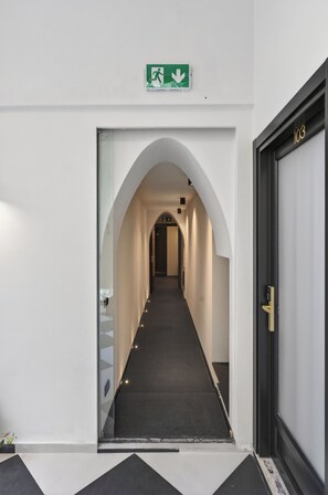 Un corridoio con un ingresso ad arco, una segnaletica di uscita di sicurezza verde e una porta con la scritta '103'.