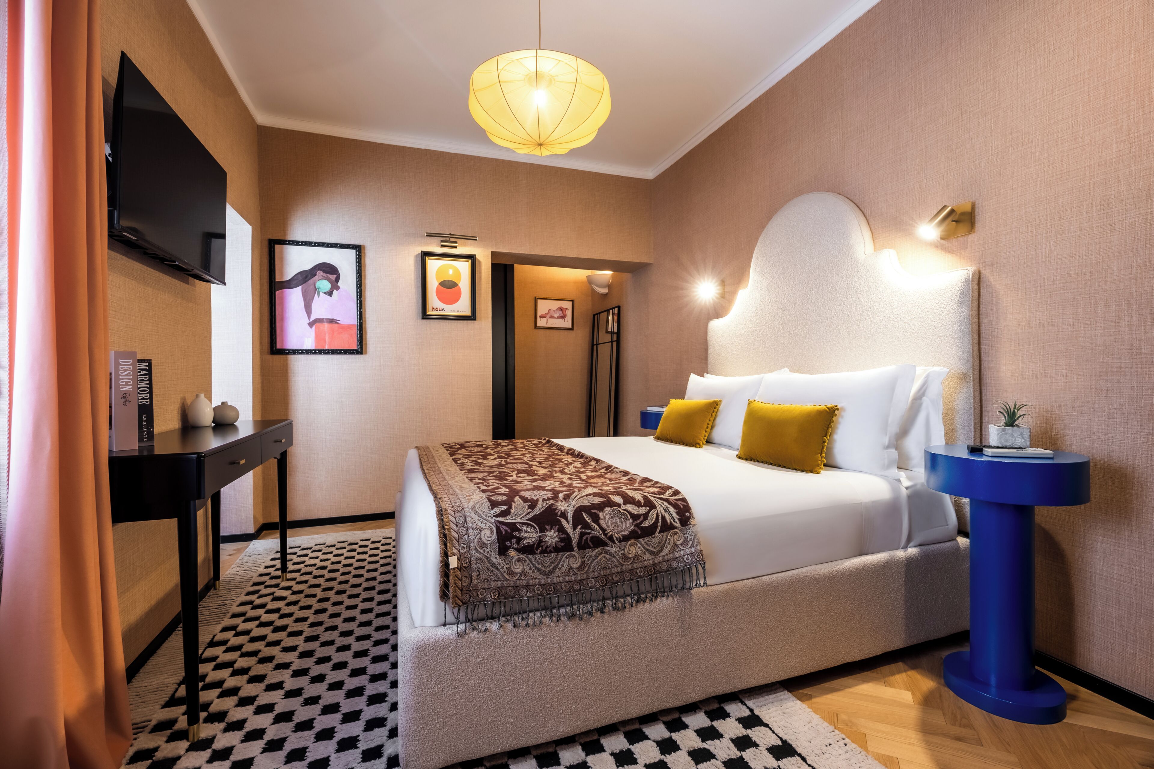 Habitación de hotel con cama, escritorio, televisor y lámpara fijada a la pared.