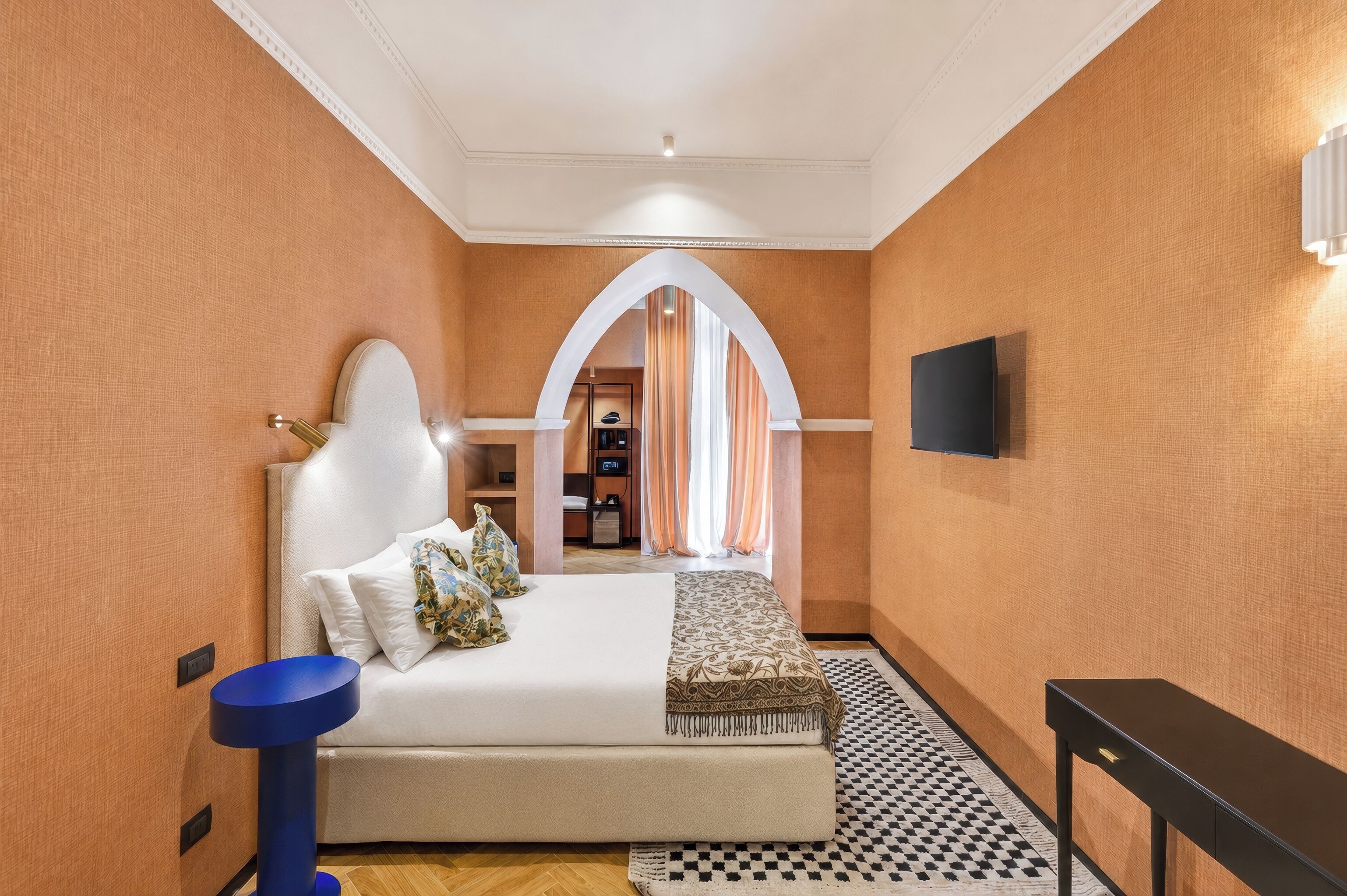 Ein Hotelzimmer mit einem Bett, einem blauen Nachttisch, einem schwarzen Nachttisch, einem Fernseher und einer gemusterten Tagesdecke.