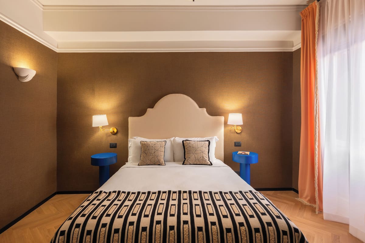 A hotel room with a large bed, two bedside lamps, a blue nightstand, and a wall-mounted light fixture.