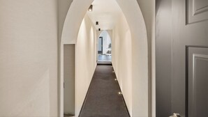 Un couloir doté d’un plafond en arc de cercle et d’un sol recouvert de moquette, qui mène à une pièce dont le sol est à carreaux.