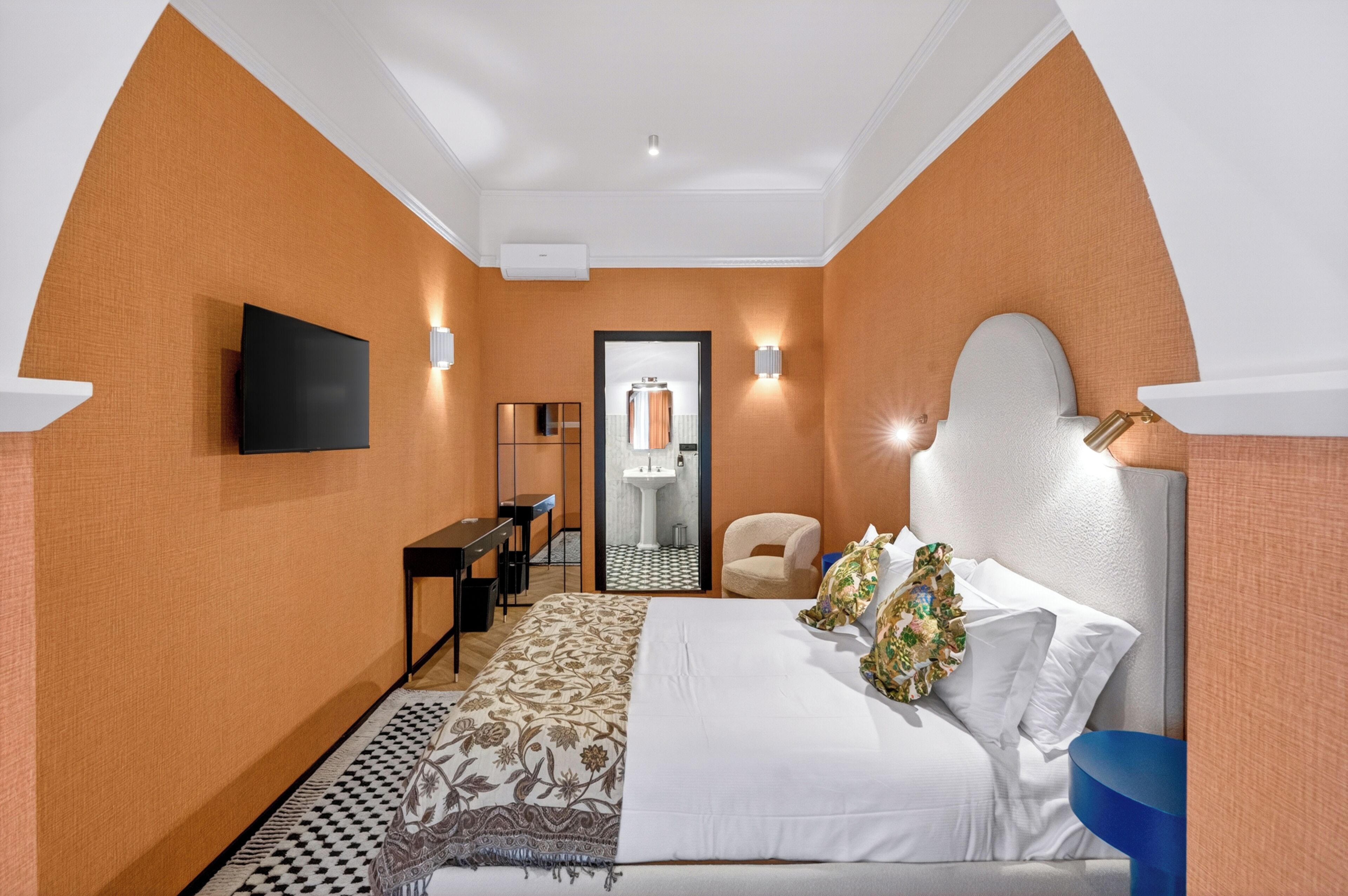 Hotelkamer met een bed, bureau, stoel, televisie en een badkamer met wastafel en spiegel.