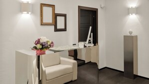 Un espace d’accueil moderne comprenant un bureau, deux chaises, un grand luminaire suspendu et des appliques murales.