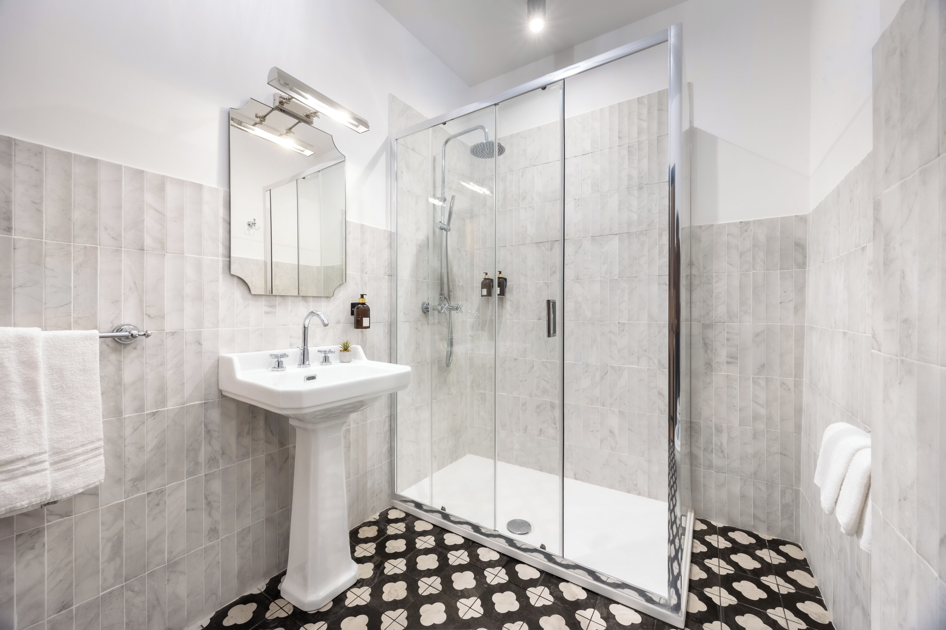 A modern bathroom with a glass-enclosed shower, a pedestal sink, and a large mirror.