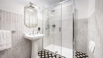 A modern bathroom with a glass-enclosed shower, a pedestal sink, and a large mirror.