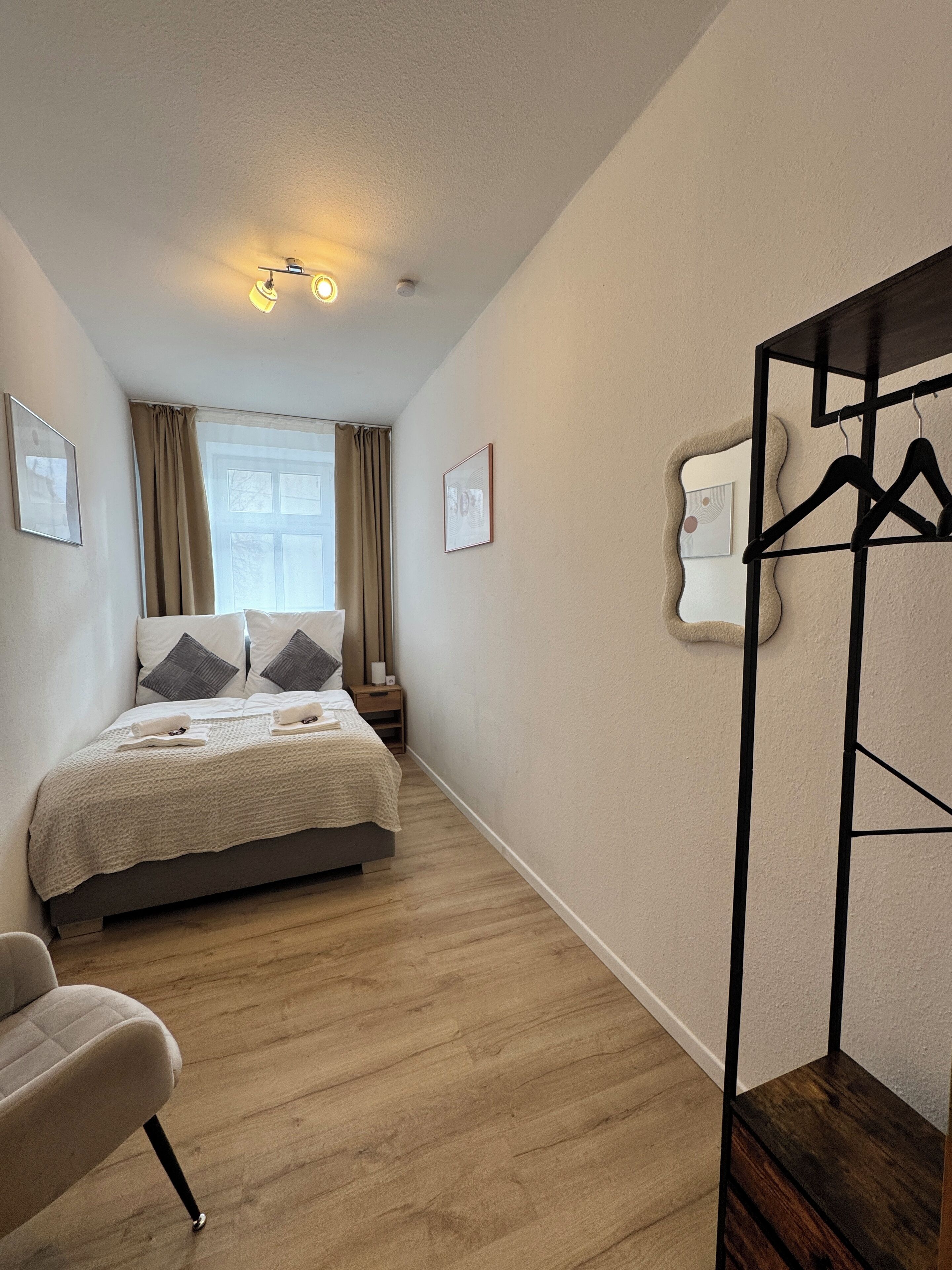 Ein Schlafzimmer mit Bett, Stuhl, Kleiderschrank und einem Fenster mit Vorhängen.