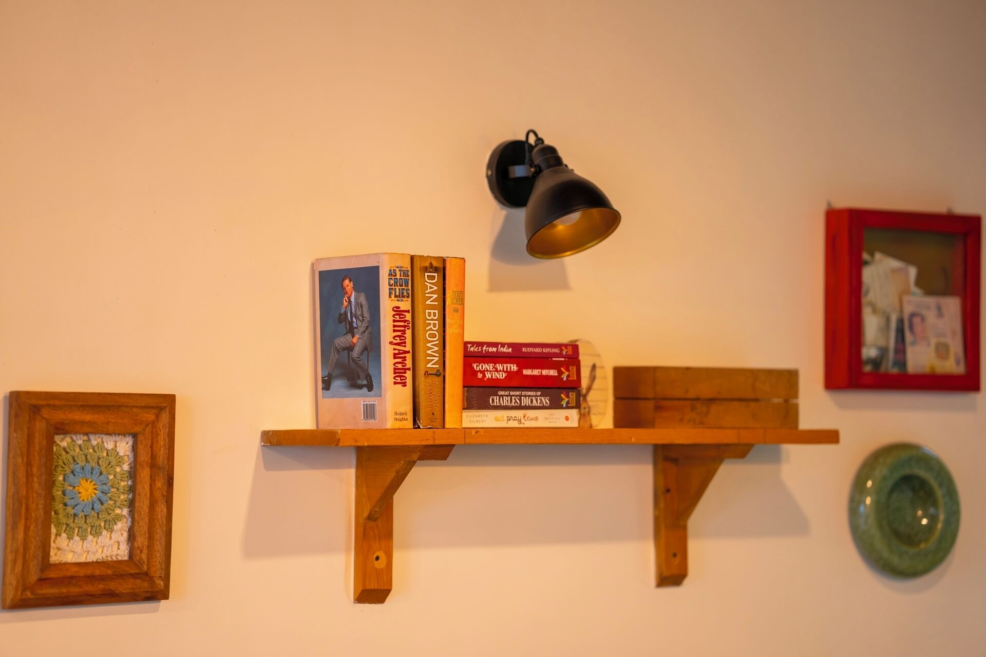 A wooden shelf with books and a wall-mounted lamp.