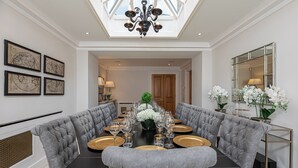 A formal dining room with a long table set for a meal, upholstered chairs, and a chandelier. - Luxury 6BR Knightsbridge house w/ Parking (London)