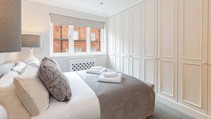 A bedroom with a bed, pillows, a window with a view of buildings, and a wardrobe. - Luxury 6BR Knightsbridge house w/ Parking (London)