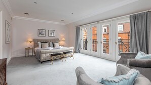 A spacious bedroom with a large bed, a sitting area with a sofa, and a balcony with a view of buildings. - Luxury 6BR Knightsbridge house w/ Parking (London)
