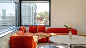 Ein modernes Wohnzimmer mit einem großen Fenster, einem runden Tisch und einer Couch mit orangefarbenen Kissen.