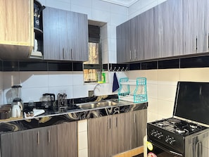A kitchen with dark wood cabinets, a black countertop, a sink, a stove, and a window above the sink.