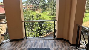 En balkon med udsigt til et stort træ og huse i baggrunden.